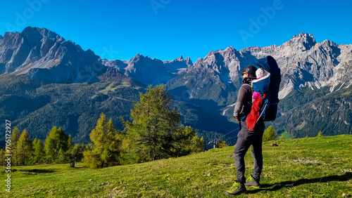 Hiker man with baby carrier with panoramic view of majestic mountain peaks of untamed Sexten Dolomites, South Tyrol, Italy, Europe. Hiking concept in Italian Alps. Looking at mount Dreischusterspitze