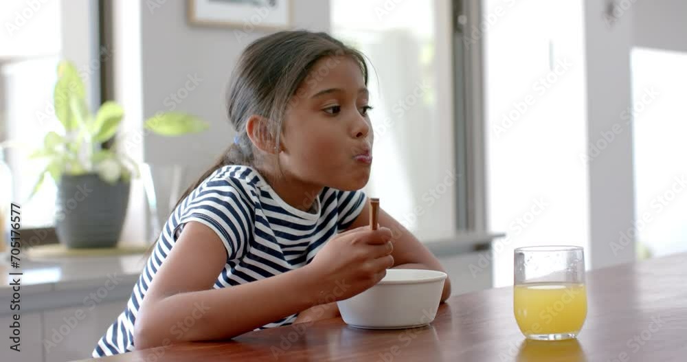 Biracial girl eating breakfast cereal sitting at island in sunny kitchen, copy space, slow motion Biracial girl eating breakfast cereal sitting at island in sunny kitchen, copy space, slow motion