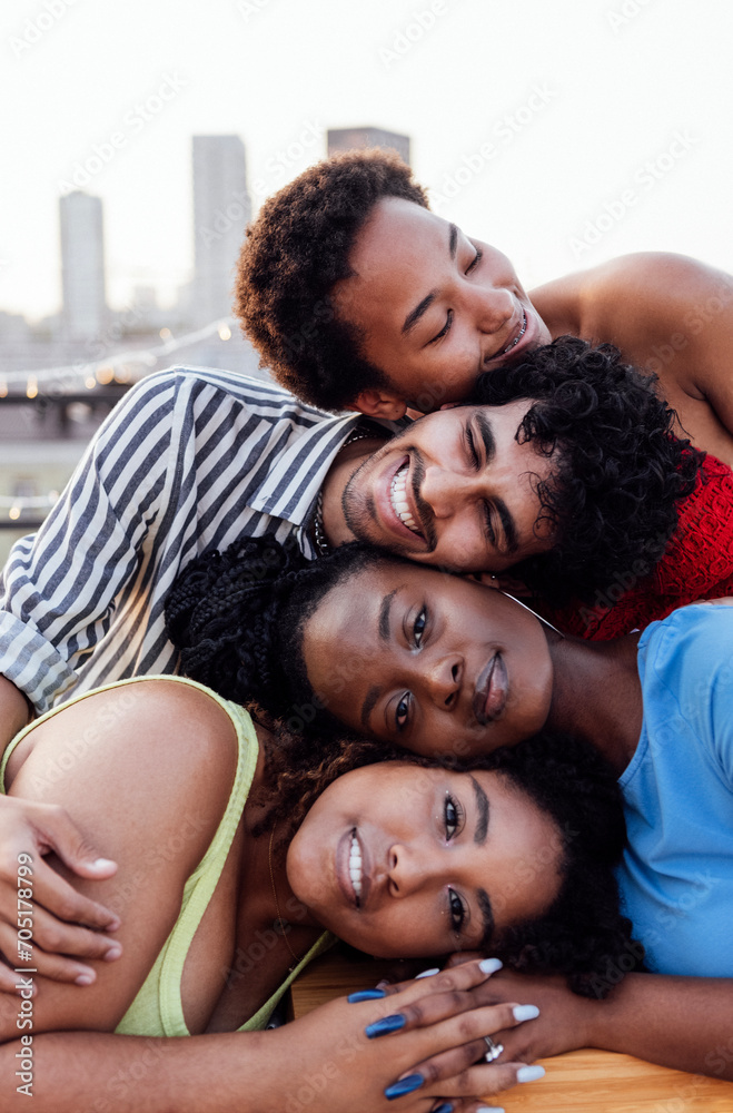 Obraz premium Four multiethnic friends put their heads on top of each other. Young people of mixed race against the backdrop of a big city.