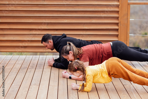 Happy family are stretching outdoors. Attractive mom, handsome dad and cute daughter doing sport exercises. Young couple and their kid are training in park. Smiling man, woman and girl 