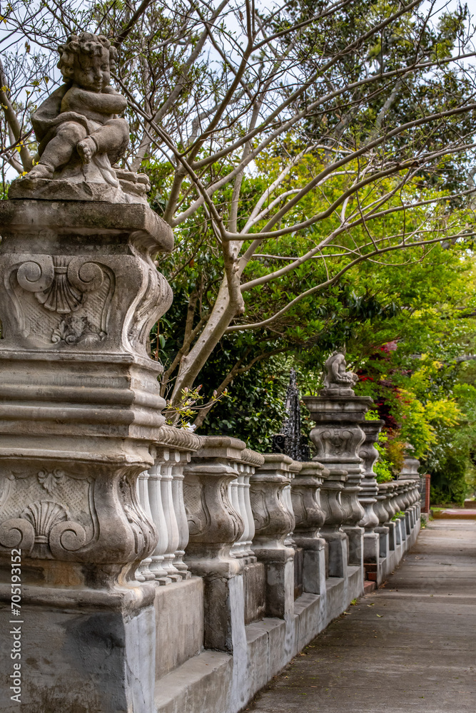 Closeup of a line of concrete ornate columns of a fence or wall with mature trees and greenery. Point of view and horizon