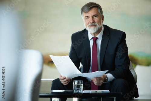 Focused serious mature businessman professional lawyer executive holding paper checking document analyzing financial report, male legal expert banker reading contract sitting at table