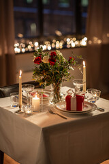 holidays, romantic date and celebration concept - close up of festive table serving for two with gift box, flowers in vase and candles burning at home on valentine's day