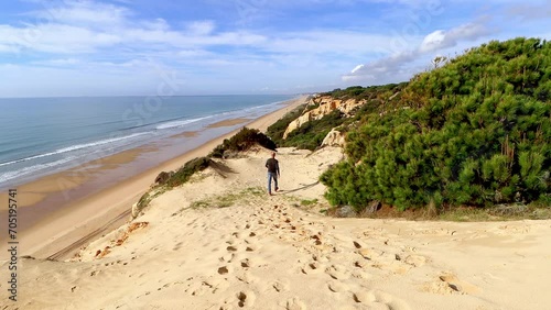 Mature man walking through the dunes of Arenosillo beach, located in Huelva, Spain. Explore the serene beauty of this coastal paradise with its sunlit sandy shores . photo