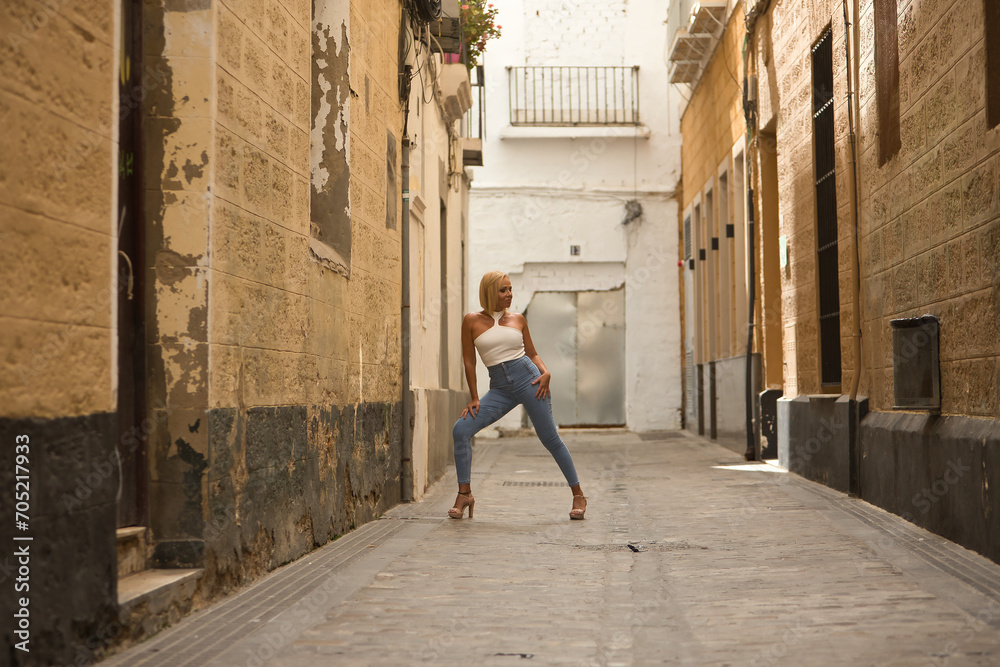 Mature, beautiful, blonde woman in white top and jeans, posing in funny attitude on a lonely city street. Concept beauty, fashion, trend, travel, maturity.