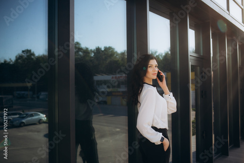 Portrait of pretty young businesswoman looking at camera while standing outdoors in city. Caucasian confident female financial consultant stands outside on stairs near office center. Business style © Roman