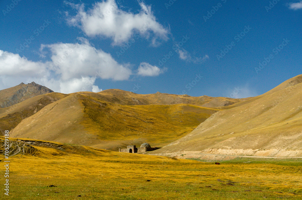 Rolling hills, Tash Rabat caravanserai in distance, golden grassland, blue sky, fluffy clouds, tranquil remote landscape