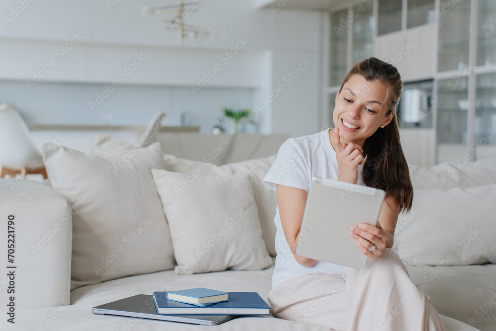 Smiling woman using a tablet on a couch, surrounded by plush cushions in a light, airy living room Smiling woman using a tablet on a couch, surrounded by plush cushions in a light, airy living room