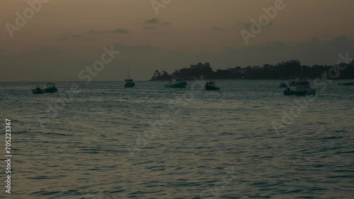 A serene establishing shot capturing fishing boats in the waters of Oistins, Barbados, bathed in the warm glow of sunset. photo