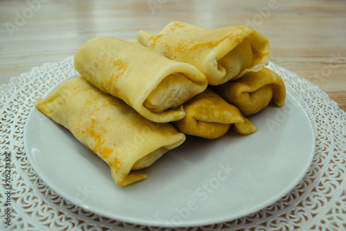 Five golden homemade pancakes with wrapped filling on a white plate