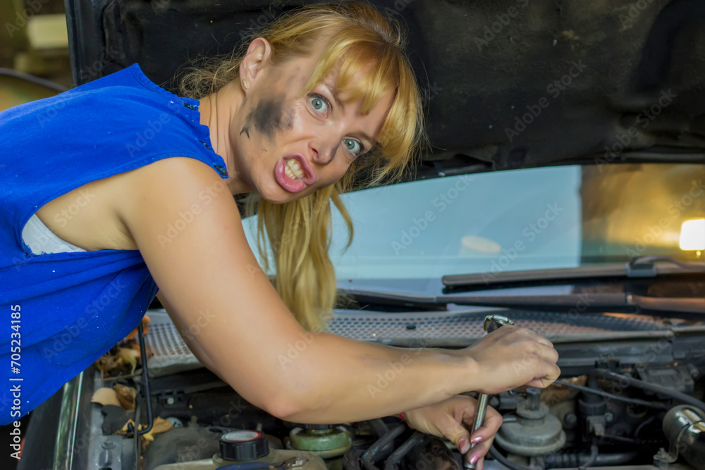 Young attractive blonde mother in blue is fixing the problem on the car. Female mechanic Young attractive blonde mother in blue is fixing the problem on the car. Female mechanic
