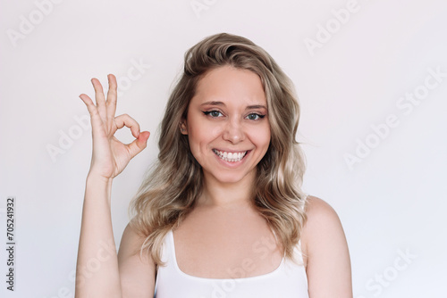 A young caucasian attractive blonde woman with wavy hair showing okay gesture with her hand isolated on a white background. Positive human emotion. The OK approval sign