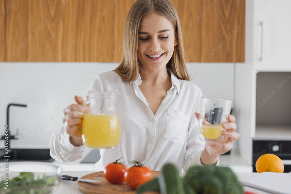 Cute blonde woman is looking at a recipe book and drinking juice in the kitchen