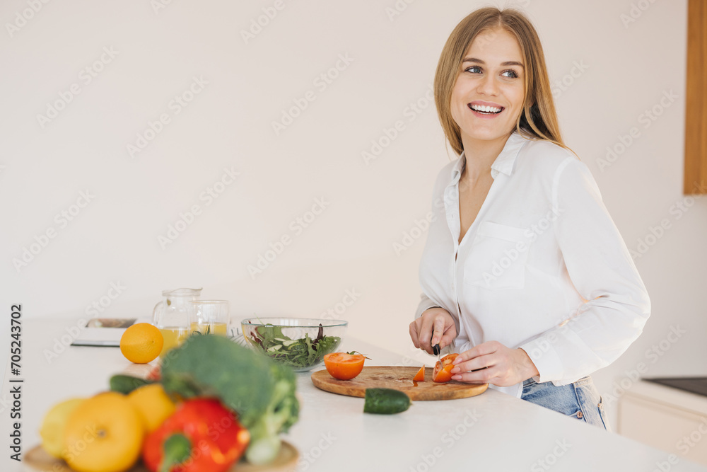 A happy cute blonde woman is preparing a salad in the kitchen