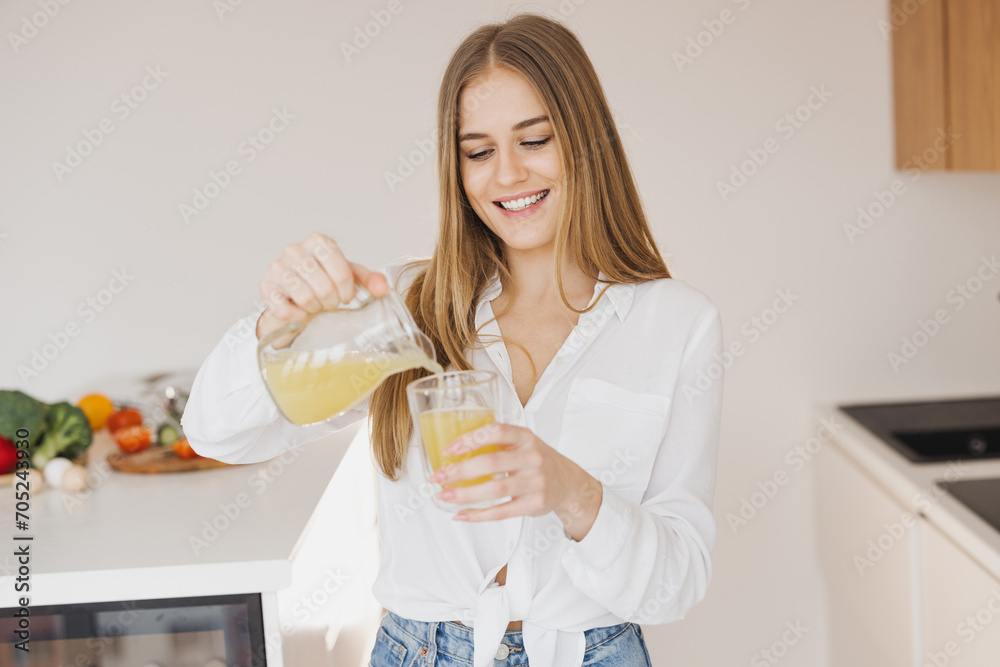 A happy cute blonde woman drinks orange juice in the kitchen A happy cute blonde woman drinks orange juice in the kitchen