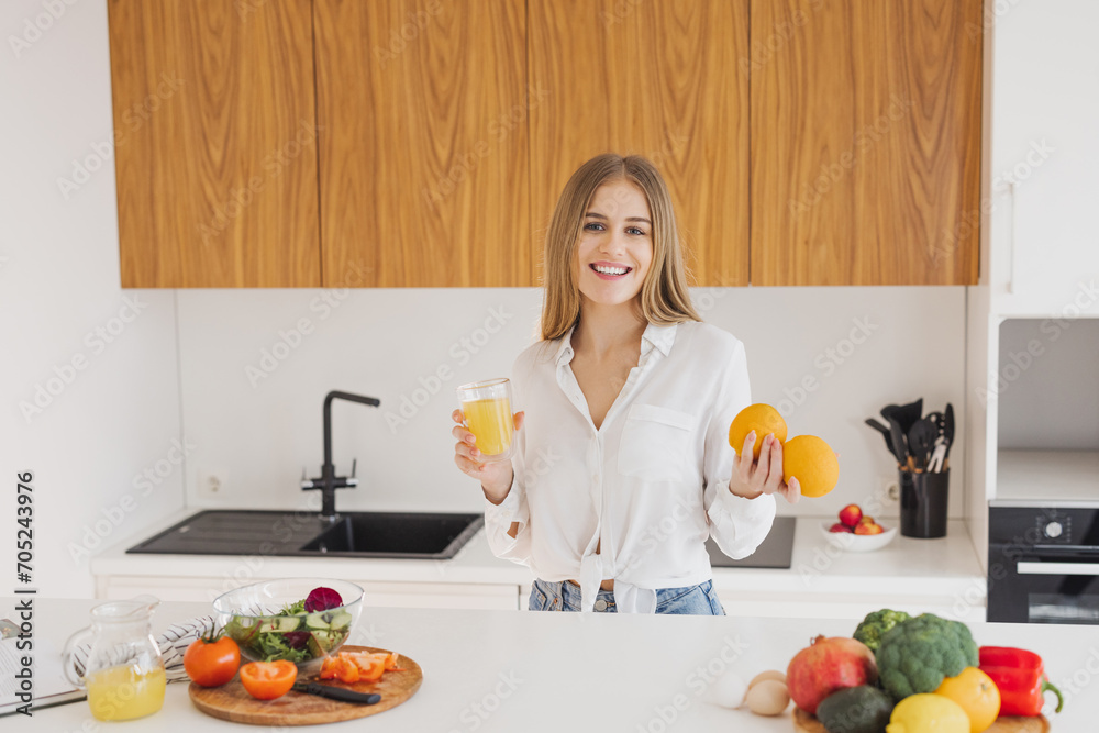 A happy blonde woman is drinking juice in the kitchen A happy blonde woman is drinking juice in the kitchen