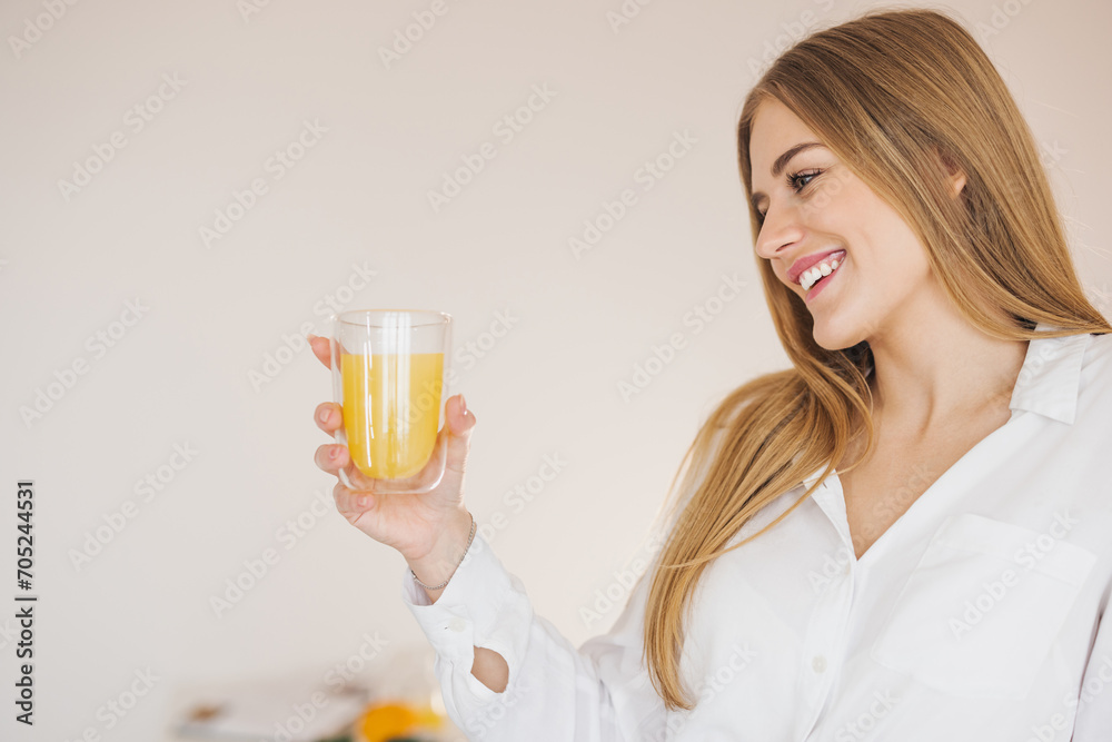 Happy and smiling blonde woman sitting on top of kitchen table and drinking orange juice among cooking ingredients. Happy and smiling blonde woman sitting on top of kitchen table and drinking orange juice among cooking ingredients.