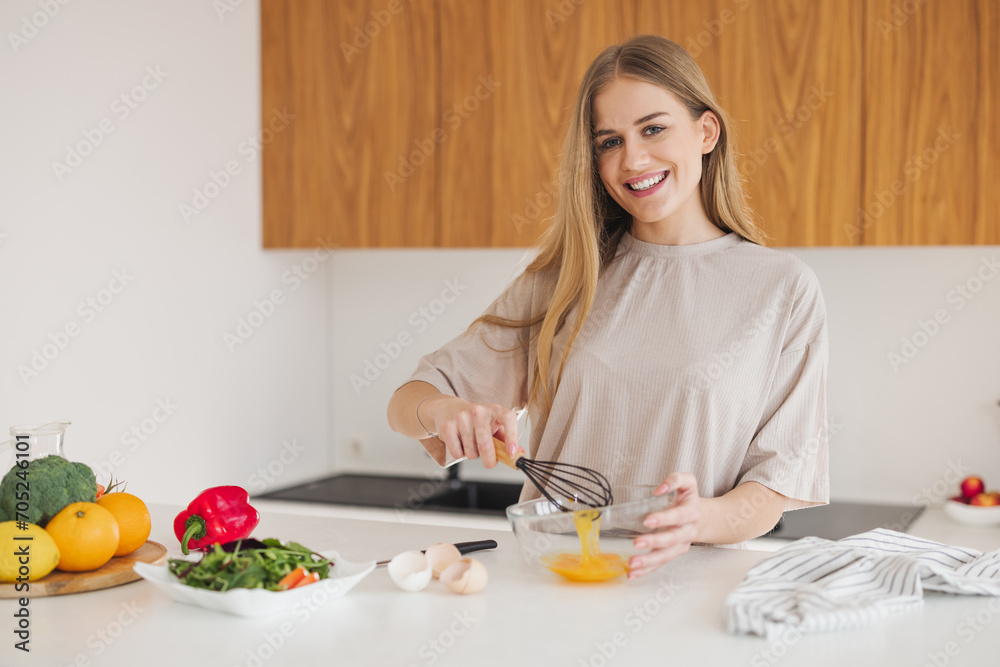 Happy pretty blonde woman in pajamas is beating eggs for breakfast in the kitchen at home. Happy pretty blonde woman in pajamas is beating eggs for breakfast in the kitchen at home.