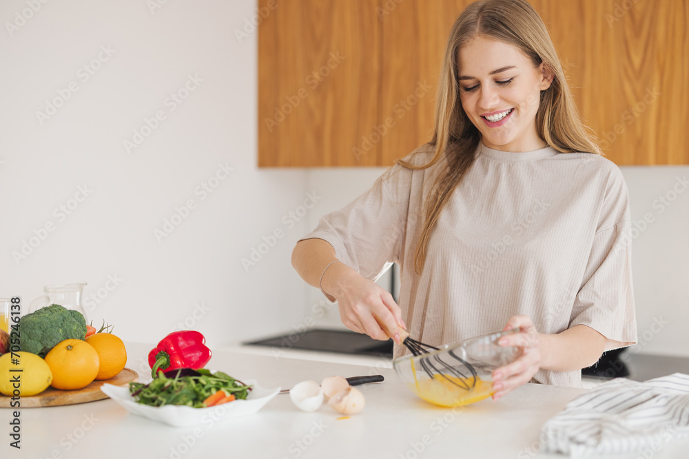 Happy pretty blonde woman in pajamas is preparing breakfast of eggs and fresh vegetables in the kitchen at home. Happy pretty blonde woman in pajamas is preparing breakfast of eggs and fresh vegetables in the kitchen at home.