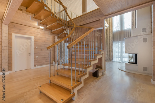 Private living room made of light wood with high ceiling. A white fireplace and a staircase .with wooden steps. photo