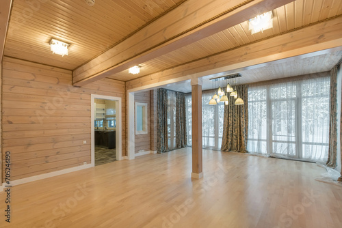 A spacious room with a light wood finish in a private house. Windows with beautiful curtains.