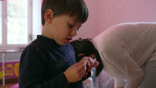 Child preparing to decorate Christmas tree with ball ornament during holiday season, young boy trying to put hook into ball