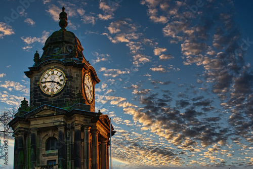 Historic clock tower silhouette against a dramatic sunset sky with scattered clouds in Lancaster.