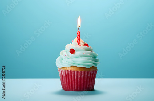Cupcake with candles and cream with cherries. Blue pastel background.