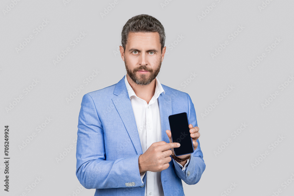 Mature man presenting phone screen. Businessman showing smartphone isolated on grey. Man in suit offer new app. Product proposal. Advertisement presentation, copy space. Promotional advertisement Mature man presenting phone screen. Businessman showing smartphone isolated on grey. Man in suit offer new app. Product proposal. Advertisement presentation, copy space. Promotional advertisement