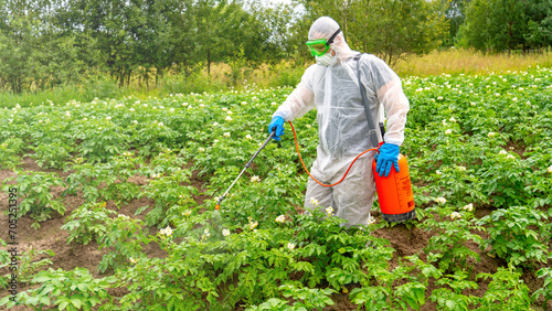 Foto Worker in protective suit treating plants with pesticides, modern agriculture an