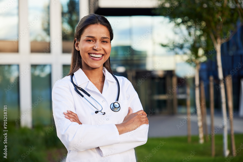 Portrait of happy female doctor standing outside at front of modern hospital Portrait of happy female doctor standing outside at front of modern hospital