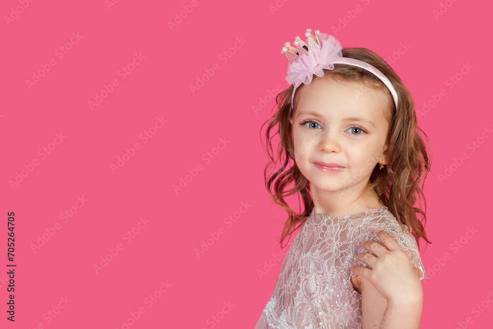 Portrait of happy little girl posing at pink background, smile looking at camera. Perfect emotional kid lady with blue eyes in pink dress, studio shot. Child image emotion concept. Copy ad text space