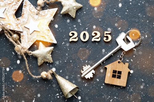 House key with keychain cottage on festive black background with stars, lights of garlands. New Year 2025 wooden letters, greeting card. Purchase, construction, relocation, mortgage, insurance photo