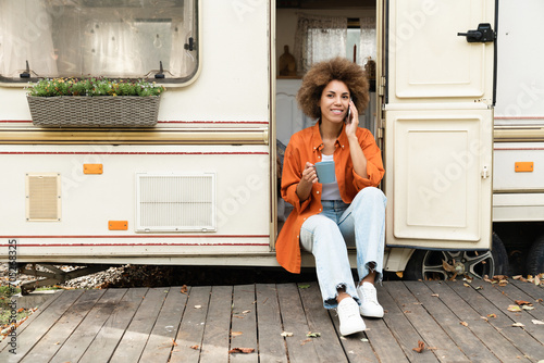 Remote job work, freelance. Young african woman solo traveler talking on cellphone with customers partners friends while travelling on van motor home on wheels trailer