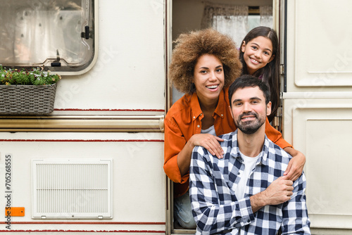 Portrait of happy family of tree with parents and small daughter traveling together by trailer motor home van home on wheels, caravanning looking at camera photo
