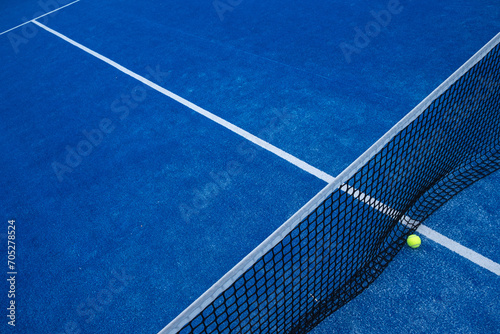 elevated view of the net of a blue paddle tennis court and a ball. © Vic