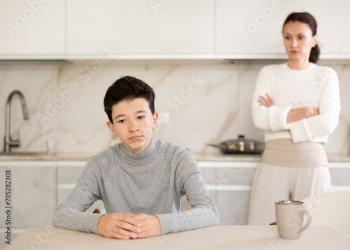 Portrait of offended teenager sitting at home while mother berating him