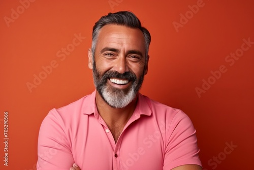 Handsome mature man with beard and mustache smiling and looking at camera while standing against orange background