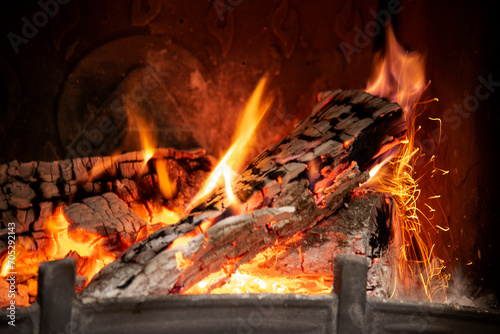 Burning ash tree logs in a home fireplace. Red flame tails  white ash  picturesque sparkles in furnace burner chamber. Space heating in cold season. Natural open fire for cozy fall and winter evening.