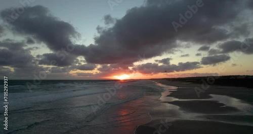 Beautiful sunset on the beach, the sun goes down over the sea while you see people kitesurfing. the clouds go fast across the sky. 