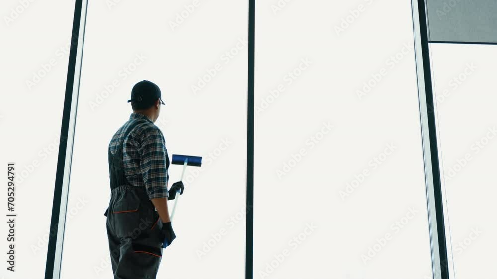 A man in uniform washes a windows with scraper. Professional home or office cleaning service A man in uniform washes a windows with scraper. Professional home or office cleaning service