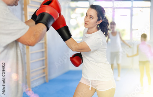 Adult woman in boxing gloves sparring with husband in gym, while preteen children, daughter and son, enthusiastically jumping rope in background. Active lifestyle and shared family sports activities © JackF