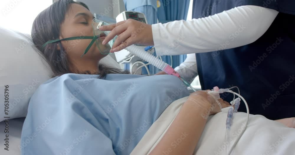 Diverse female patient in hospital bed and female doctor putting oxygen mask on her, slow motion