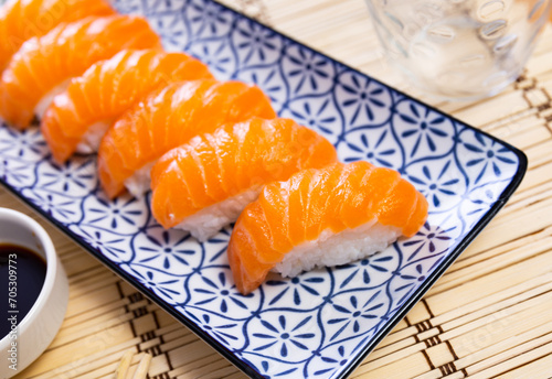 Close-up unique and delicious pieces of Norwegian salmon nigiri on porcelain plate on bamboo mat.