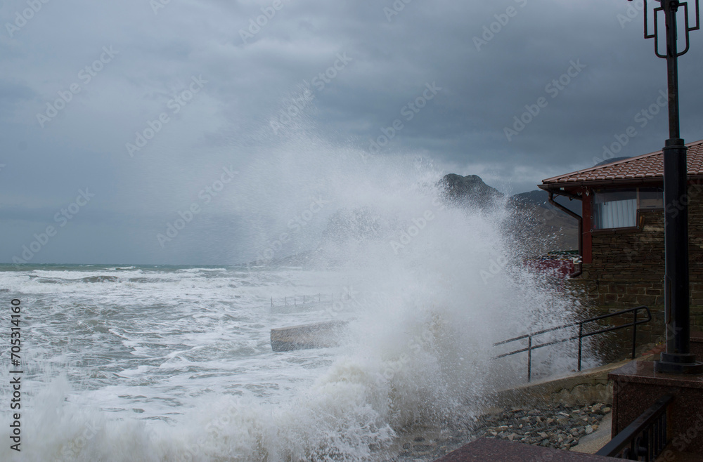 A storm in Koktebel. Large waves crash against the parapet. A sky with dark clouds.