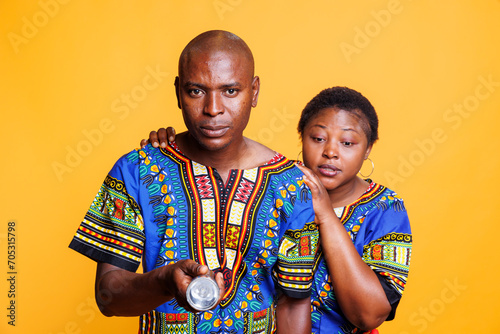 Frightened african american man and woman couple illuminating with flashlight. Confident husband with spotlight searching dark and looking at camera while terrified nervous wife hiding behind back