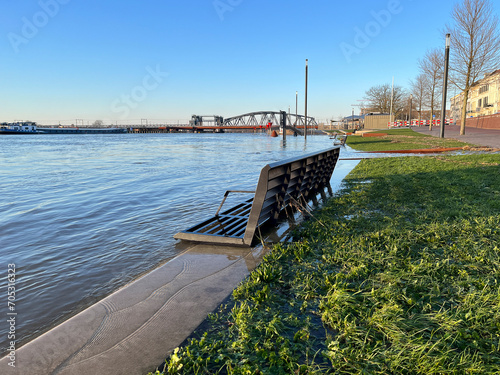 Bench almost under water during winter high water level showing partly flooded boulevard from river IJssel at sunset photo