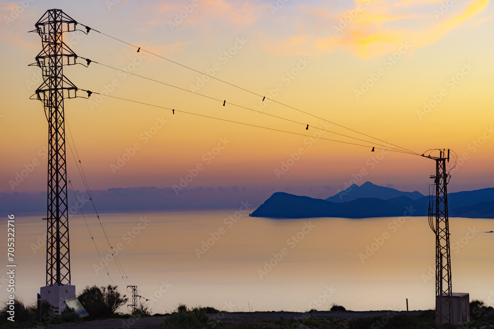 High voltage towers on coast at sunset