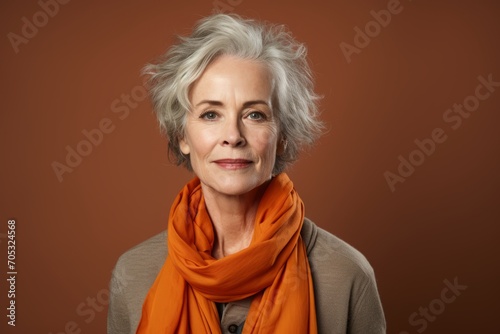 Portrait of a beautiful senior woman with orange scarf on brown background