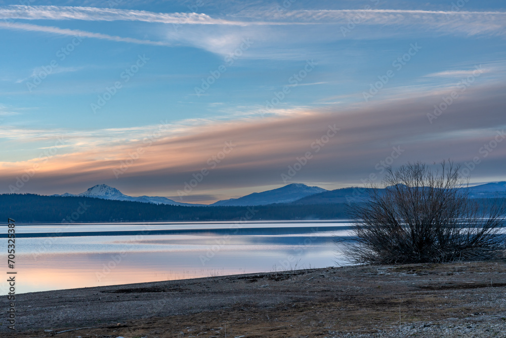 Dramatic image of lake Almanor with Mt Lassen in background and calm reflecting waters and beach in foreground in the California mountains.